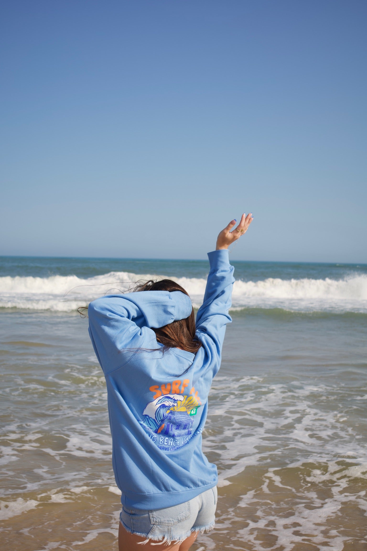Person wearing a blue sweatshirt with a surf design on a beach